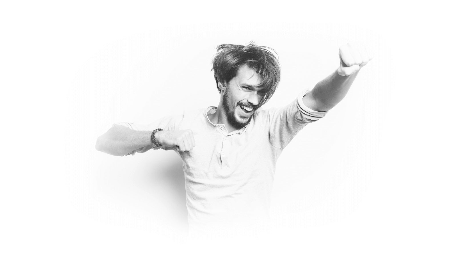 Black and white portrait of a cheerful man standing with his hands raised against the white wall